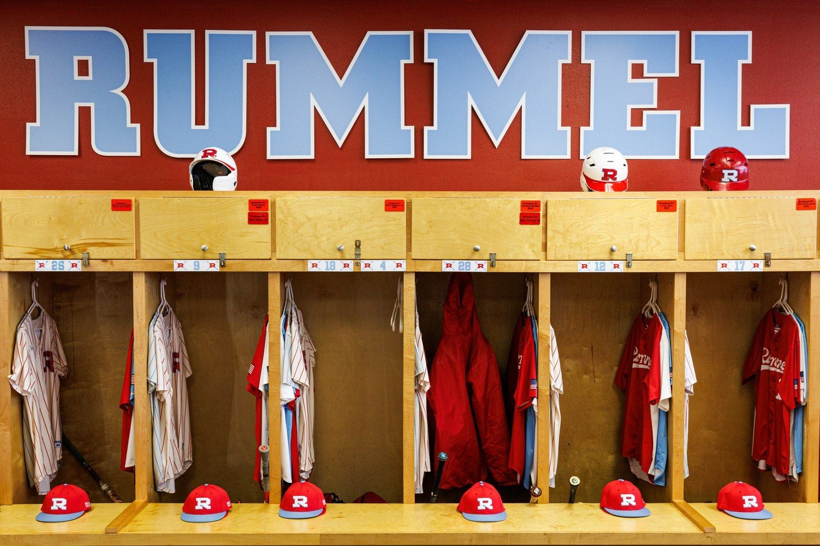 Wooden locker stalls with jerseys and red caps under a RUMMEL sign