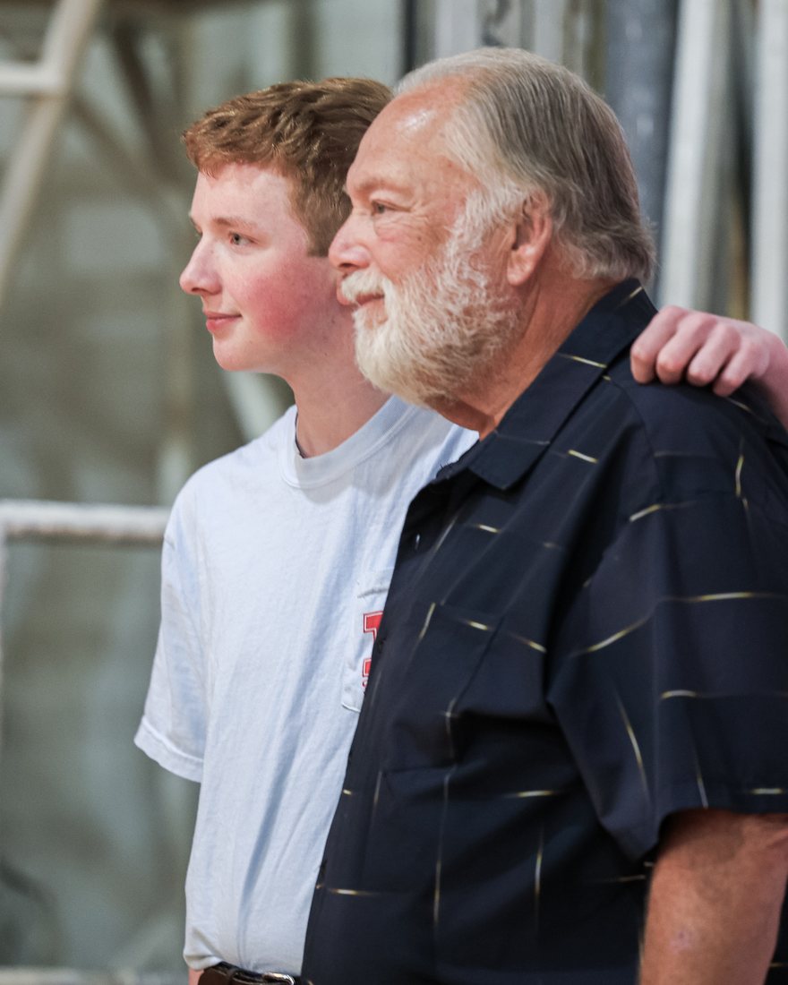 A Rummel graduate with his arm around his son in front of the R backdrop