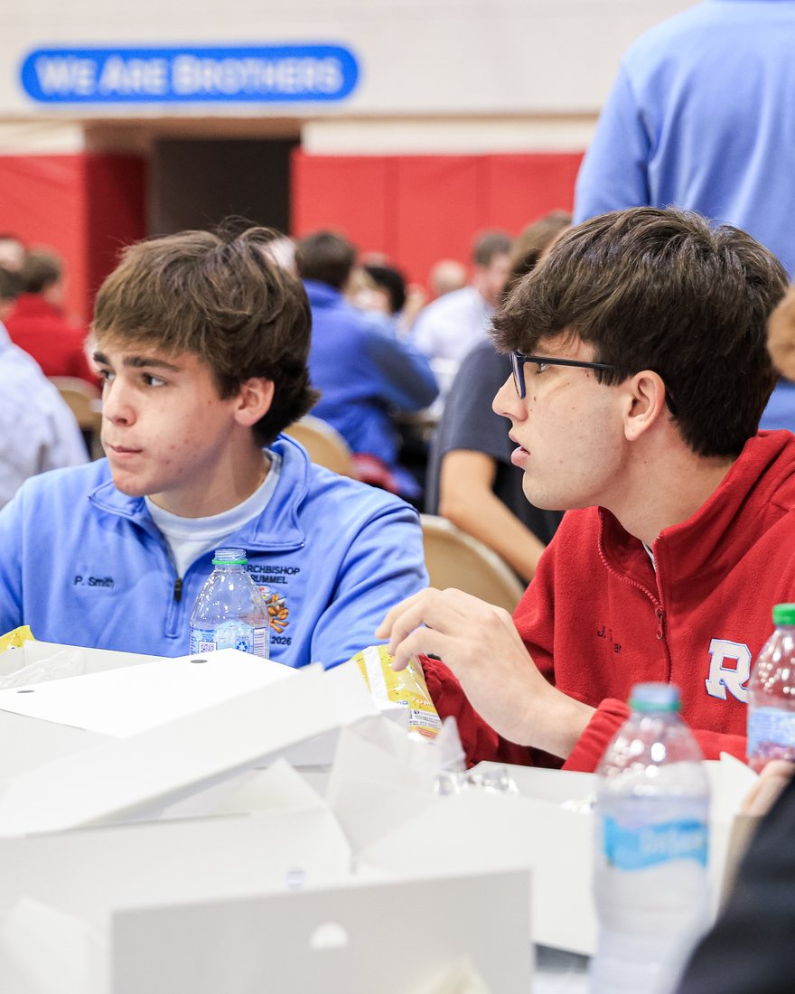 Two Raiders talking at lunch under the We Are Brothers banner