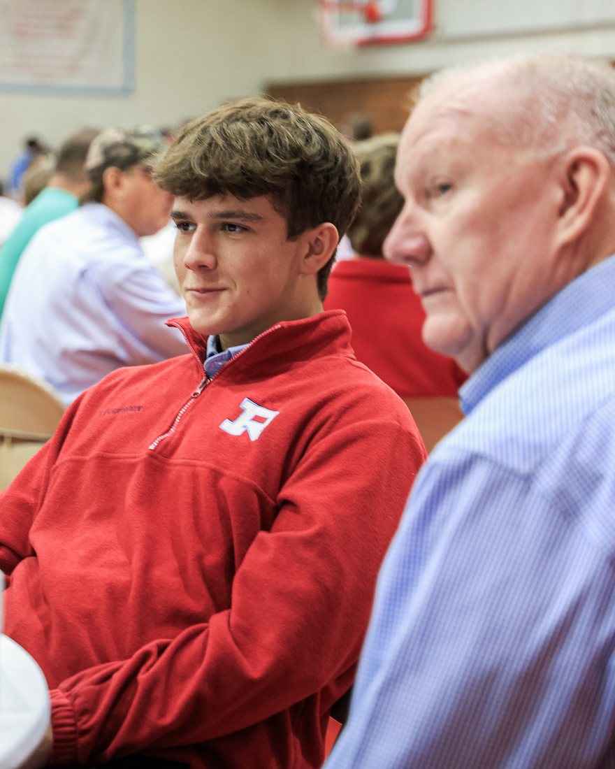 A student in a red Rummel pullover beside his grandfather at the table
