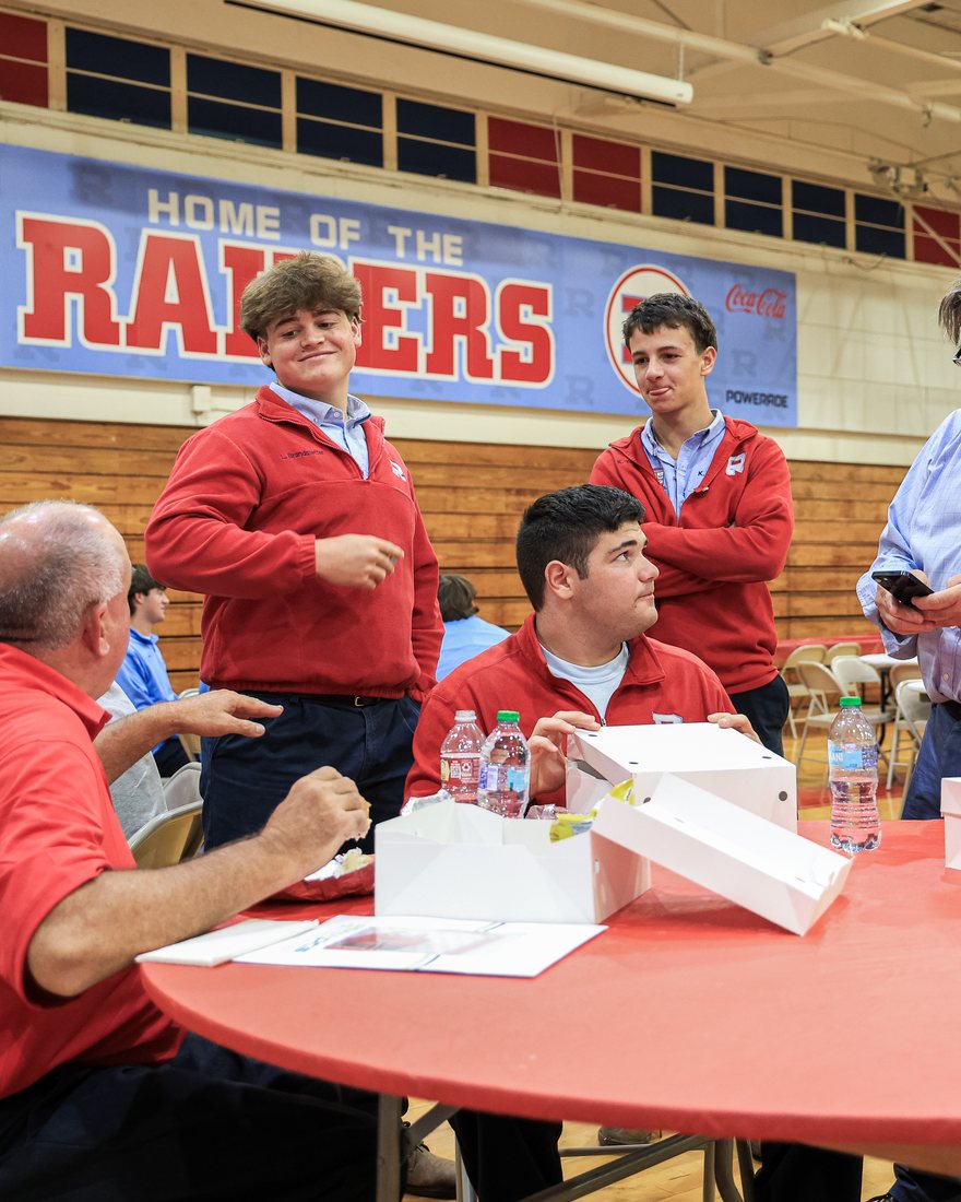 Students and families at a table under the Home of the Raiders banner