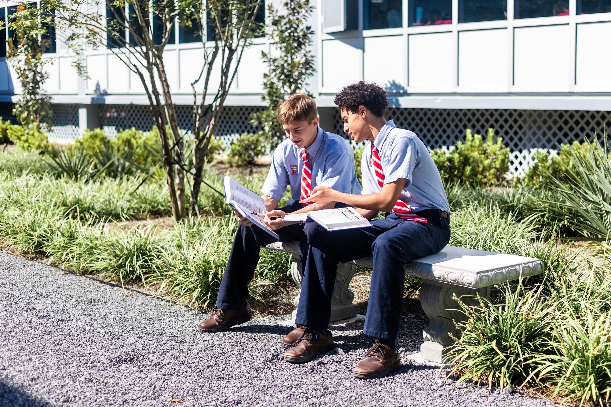 Two Rummel students reading together on a bench in the courtyard